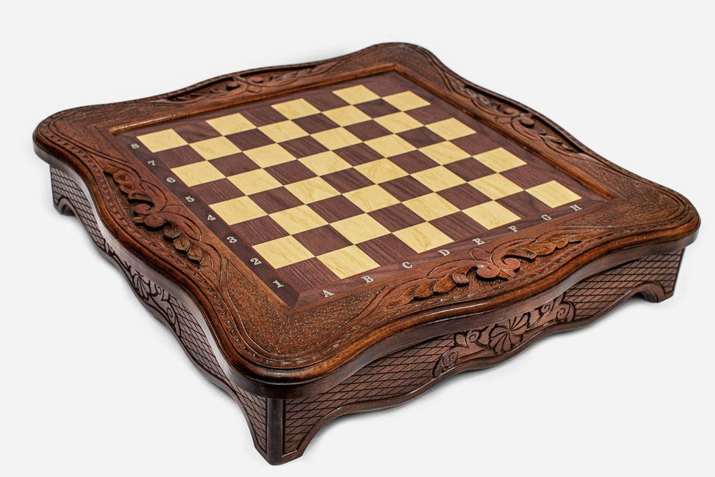 Empty carved wooden chess board showing the scalloped frame and checkered playing surface