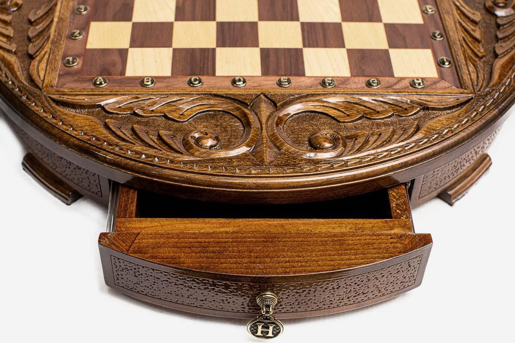 Close-up of the round chess set's open storage drawer with ornate brass pull handle and carved frame