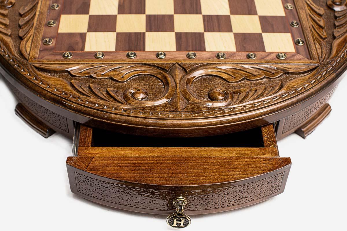 Close-up of the round chess set's open storage drawer with ornate brass pull handle and carved frame