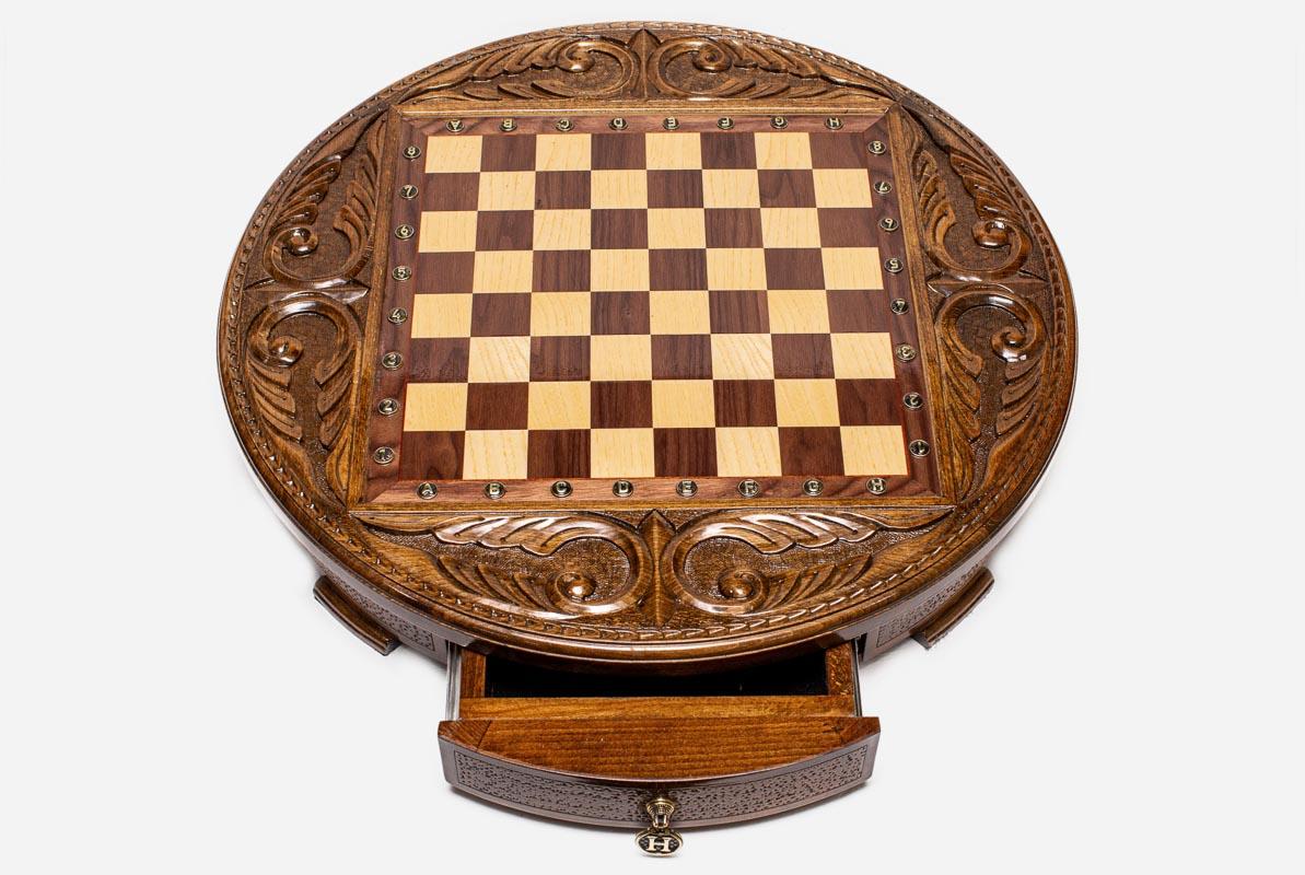 Top-down view of the round wooden chess board with brass coordinate markers and open storage drawer
