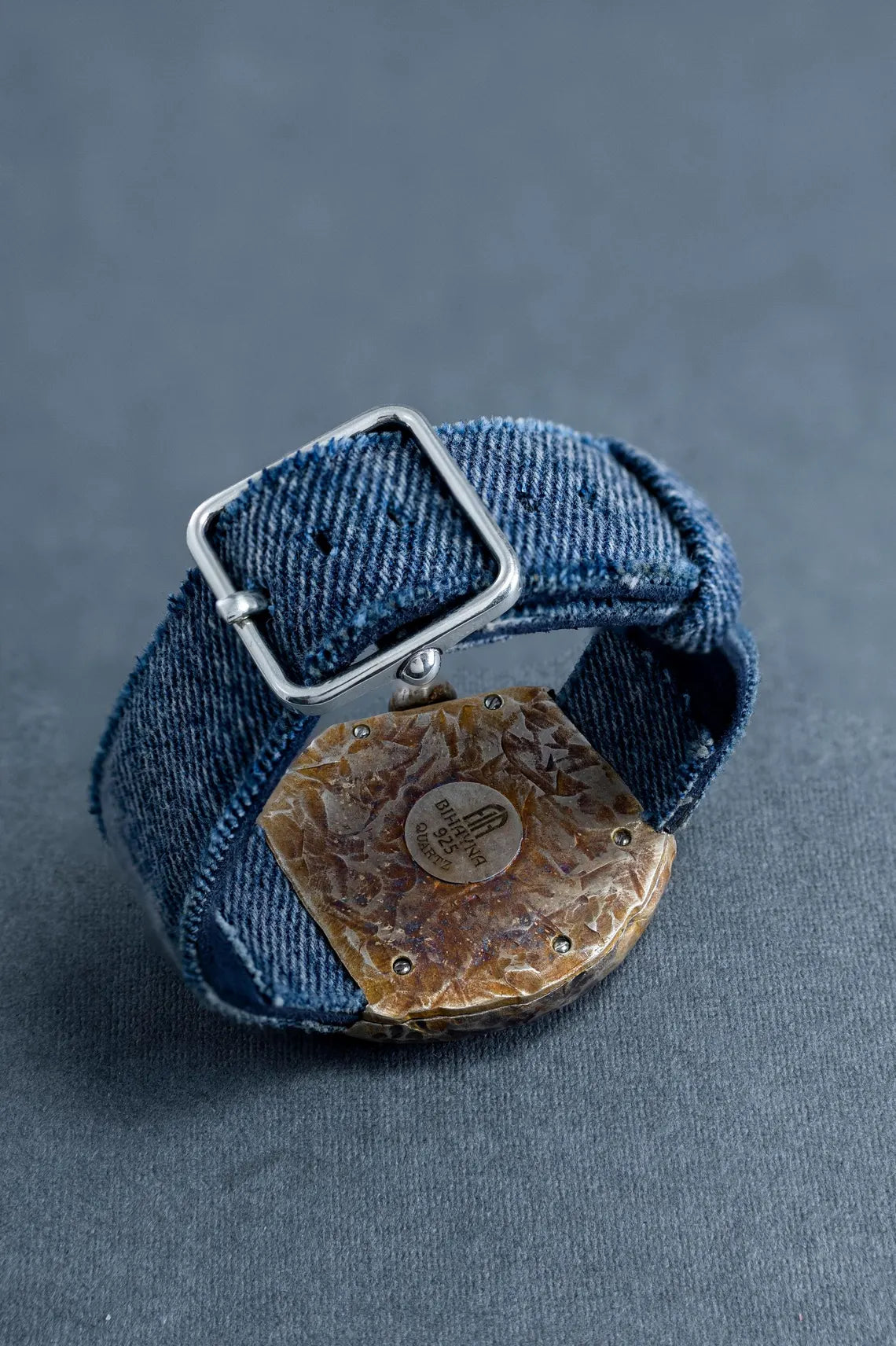 Denim bracelet with a metal clasp on a gray background