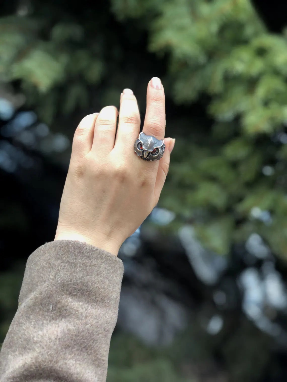 Hand wearing a silver ring with a blurred green background