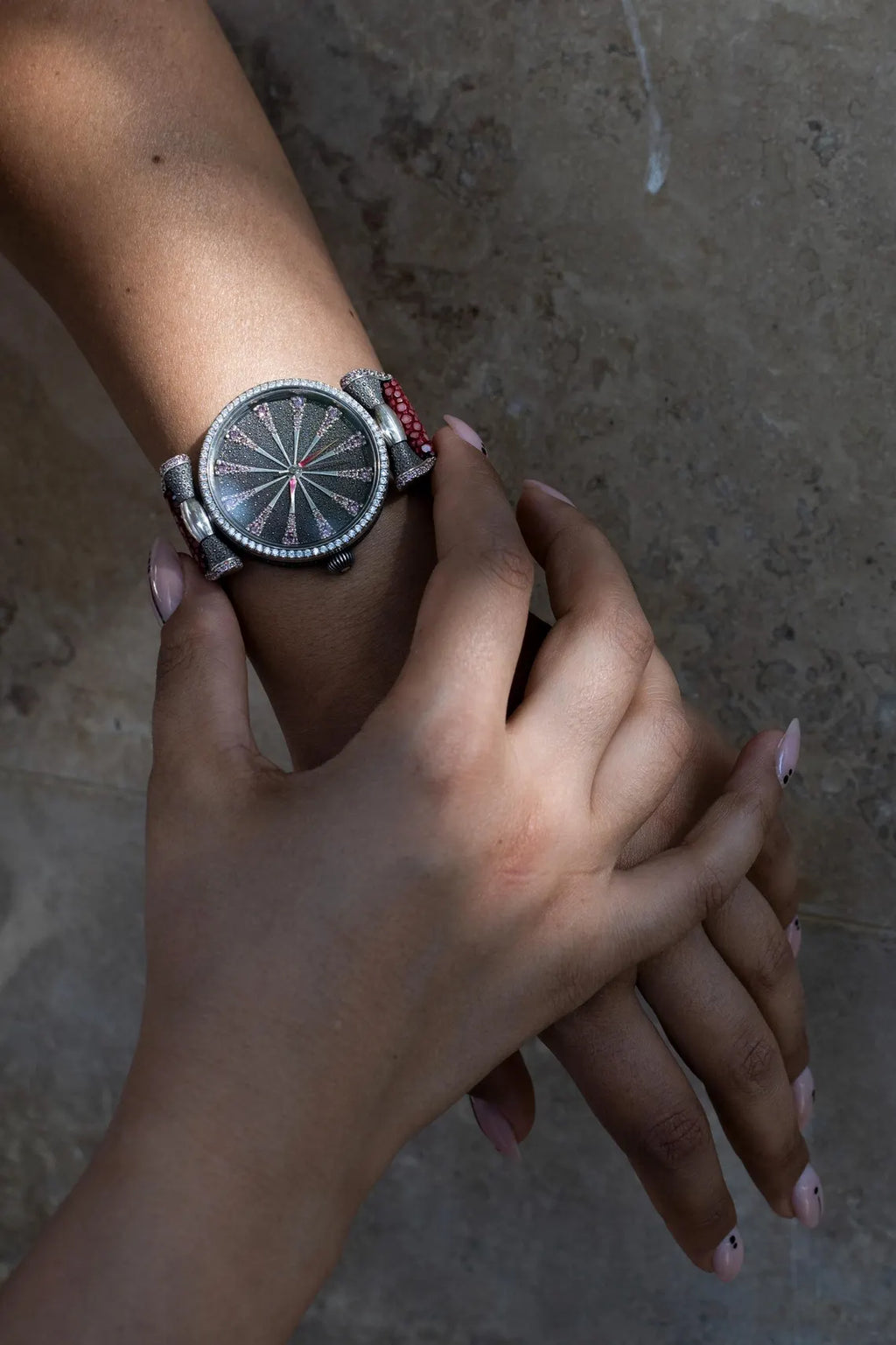 Close-up of a hand wearing a silver watch with a textured face on a neutral background