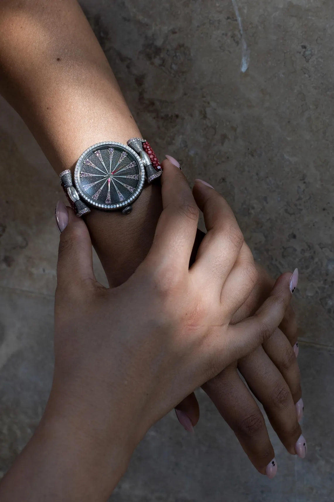 Close-up of a hand wearing a silver watch with a textured face on a neutral background