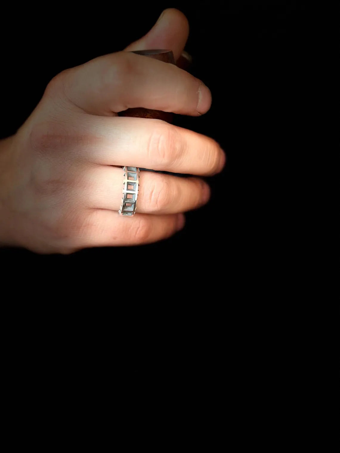 Hand wearing a silver ring on a black background