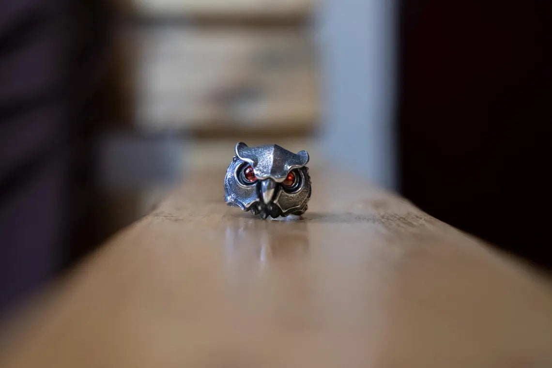 Silver owl-shaped ring on a wooden surface with a blurred background