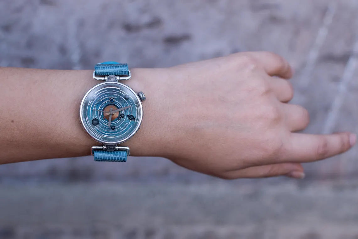 Hand wearing a watch with a blue strap on a blurred background