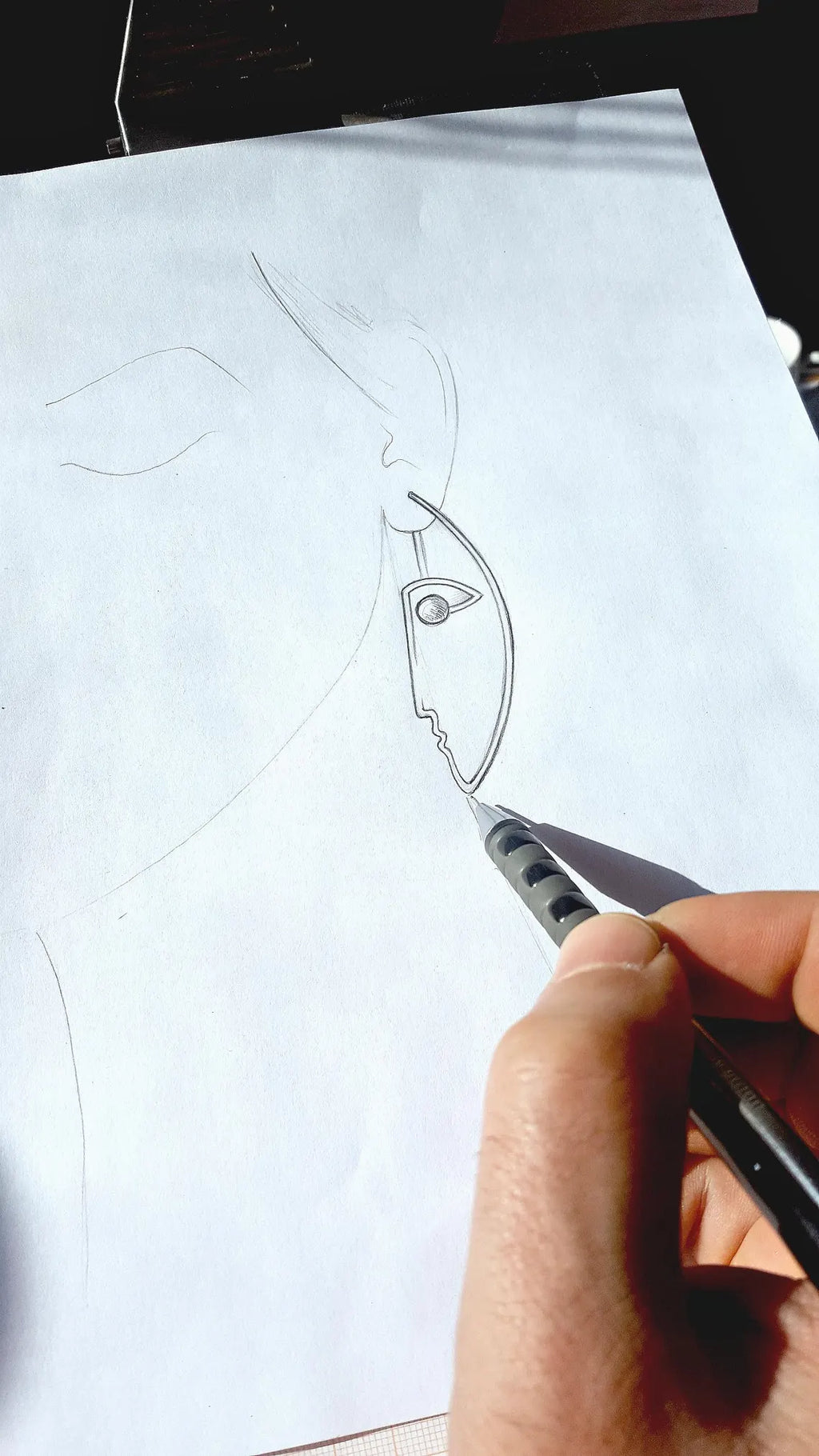 Hand holding a pen over a piece of paper with a design sketch.