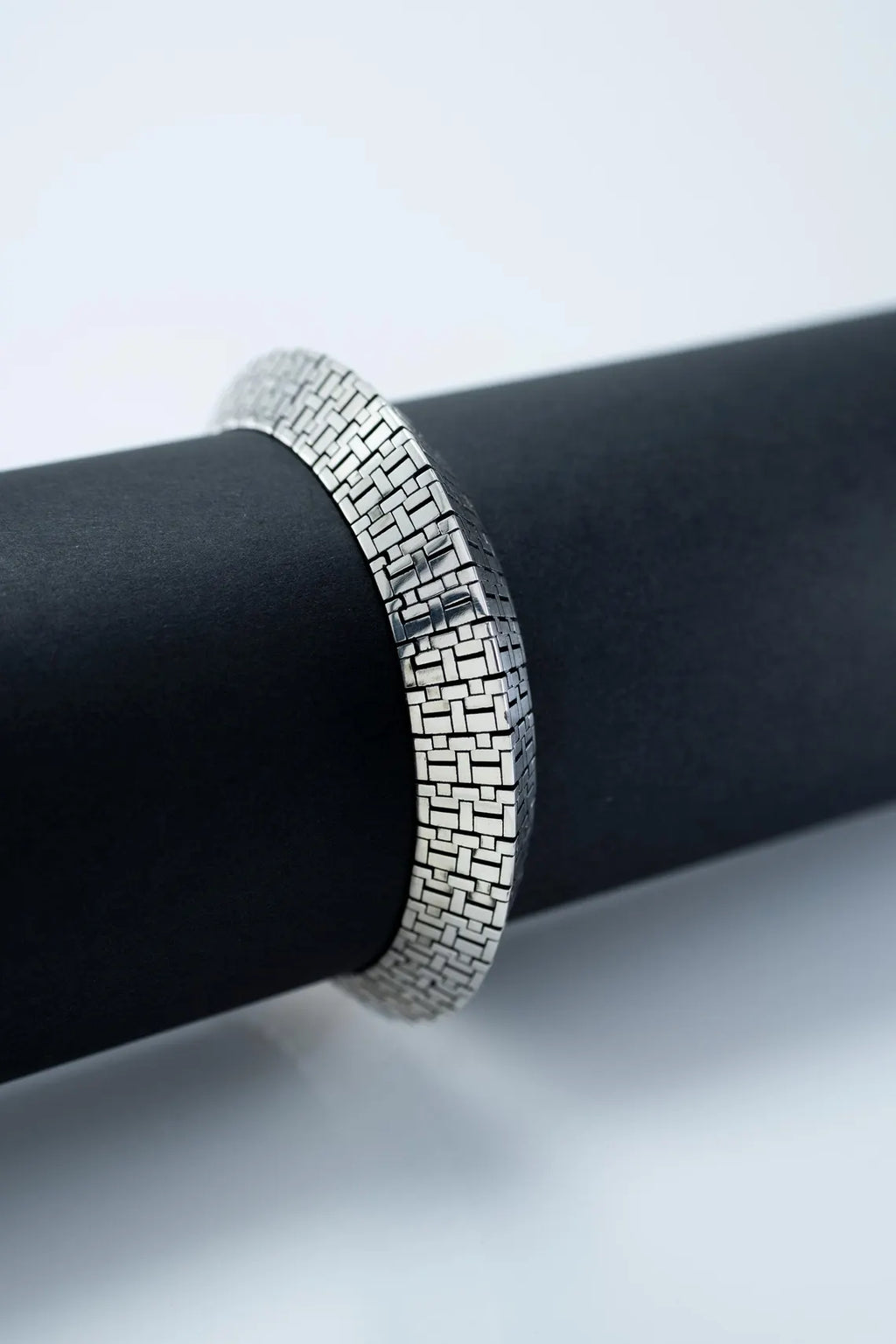 Silver bracelet on a black cylindrical object with a white background