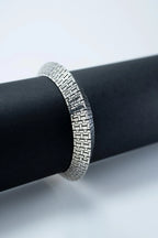 Silver bracelet on a black cylindrical object with a white background