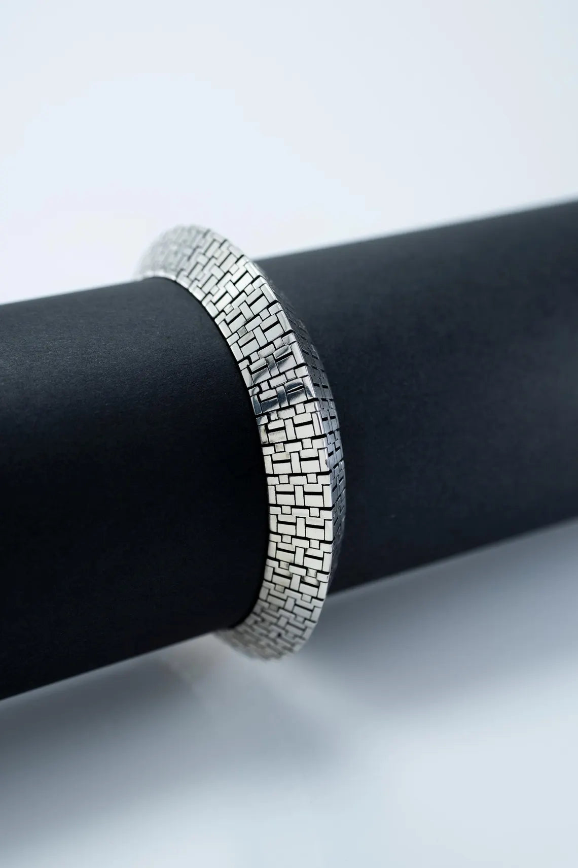 Silver bracelet on a black cylindrical object with a white background