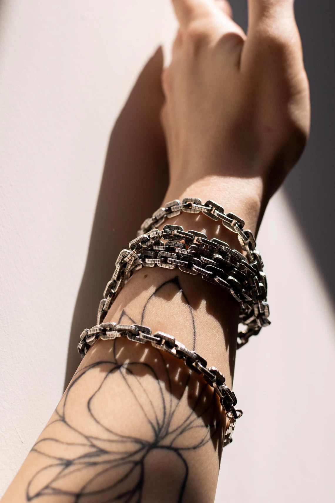 Hand wearing multiple chain bracelets on a neutral background