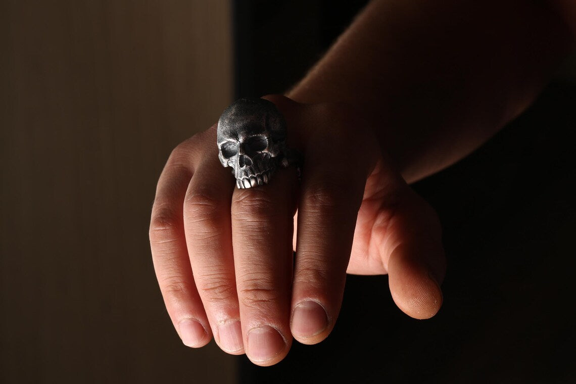 Hand holding a skull-shaped ring against a dark background