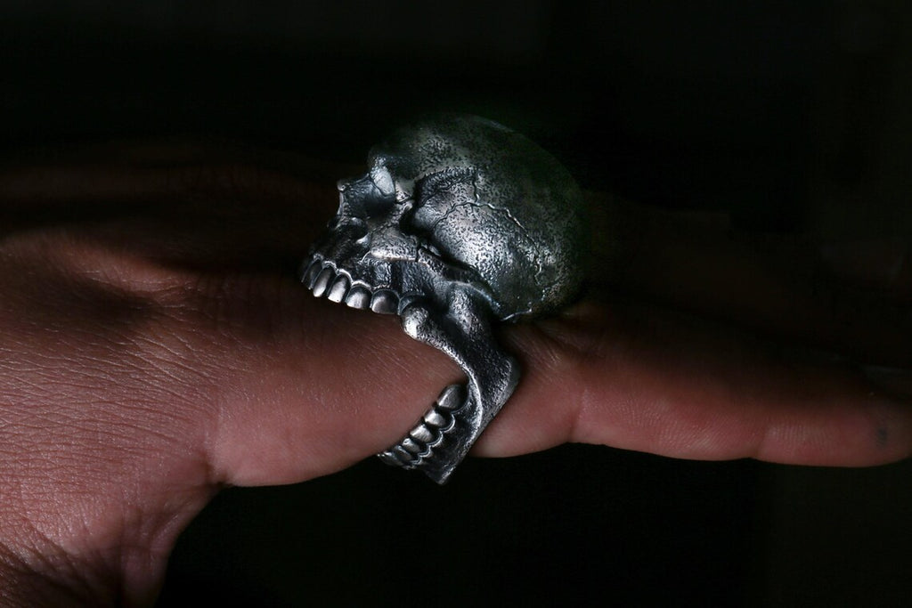Silver skull ring on a finger against a dark background