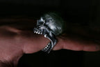 Silver skull ring on a finger against a dark background