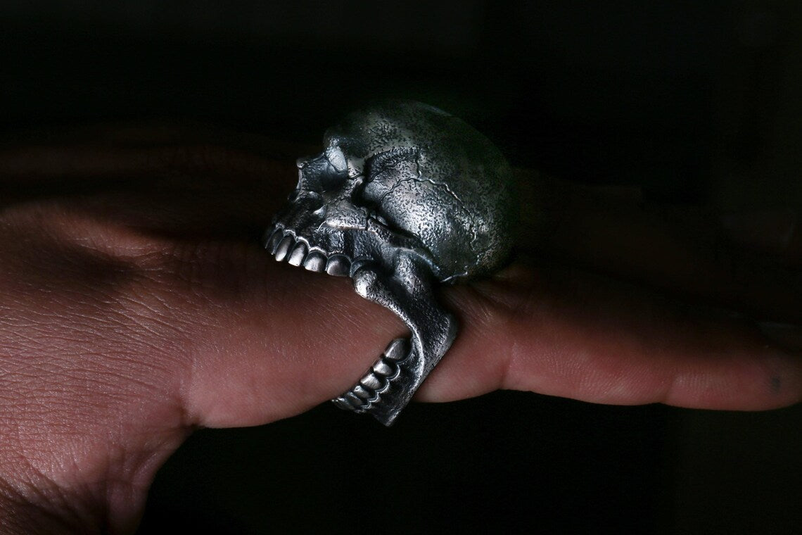 Silver skull ring on a finger against a dark background