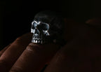 Silver skull ring on a finger against a dark background