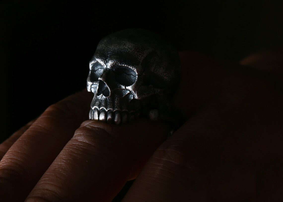 Silver skull ring on a finger against a dark background