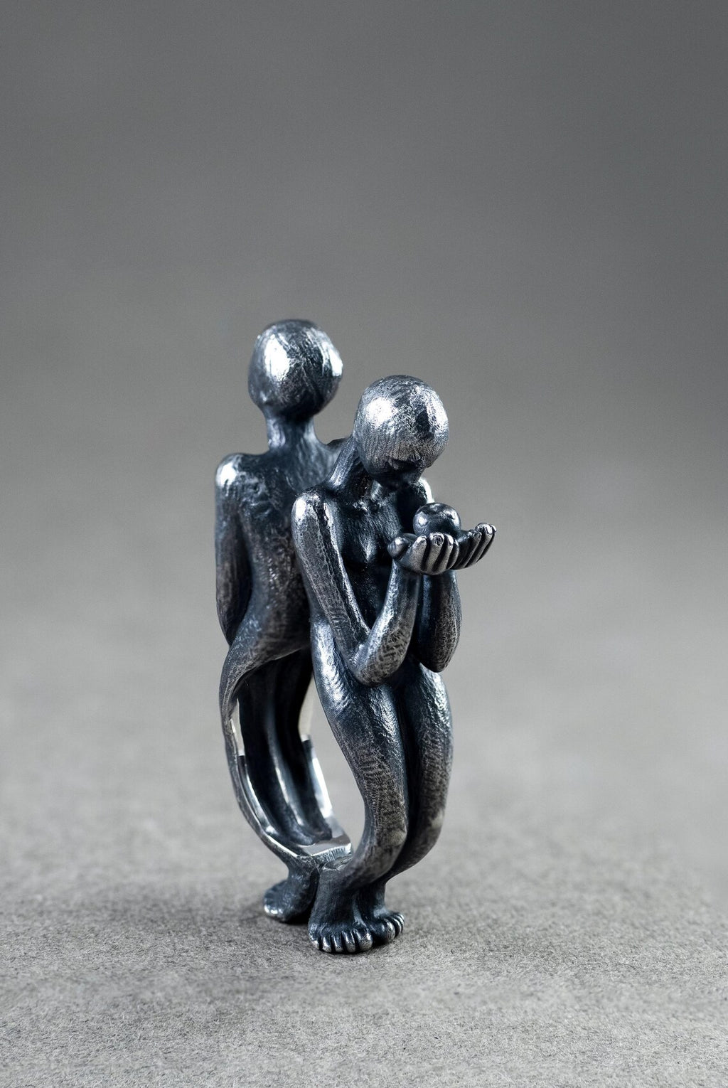 Metallic sculpture of two people embracing on a gray background