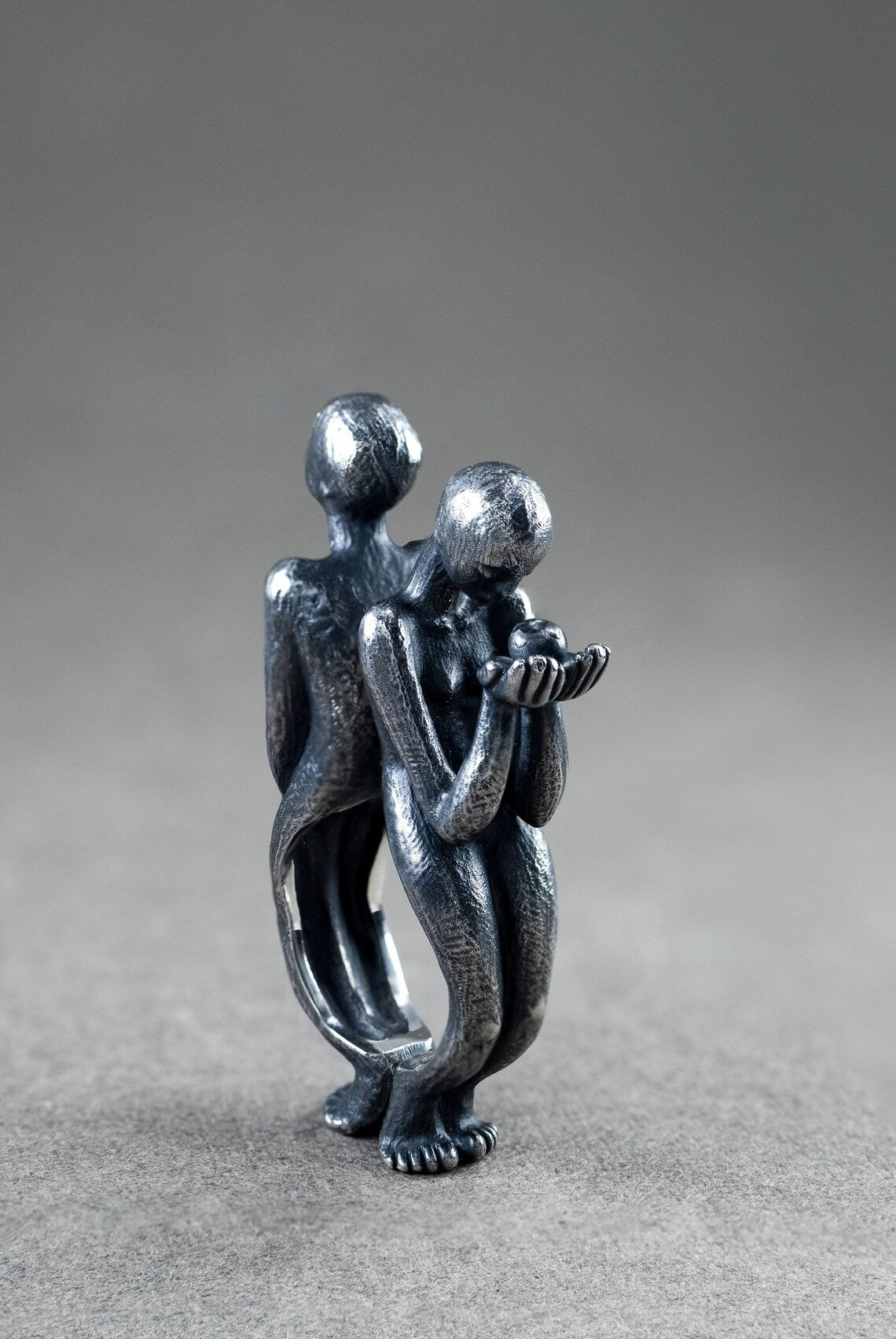 Metallic sculpture of two people embracing on a gray background