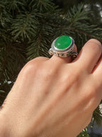 Hand wearing a green stone ring with silver band against a blurred green background