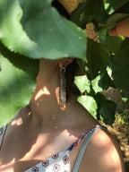 Person wearing colorful earrings with green leaves in the background
