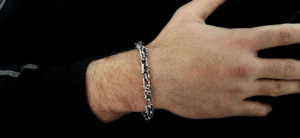 Hand wearing a silver chain bracelet on a black background