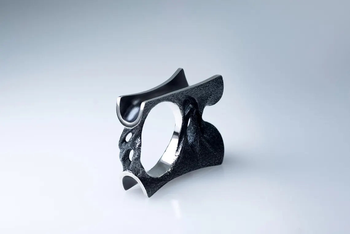 Black metallic ring with a unique design on a light gray background