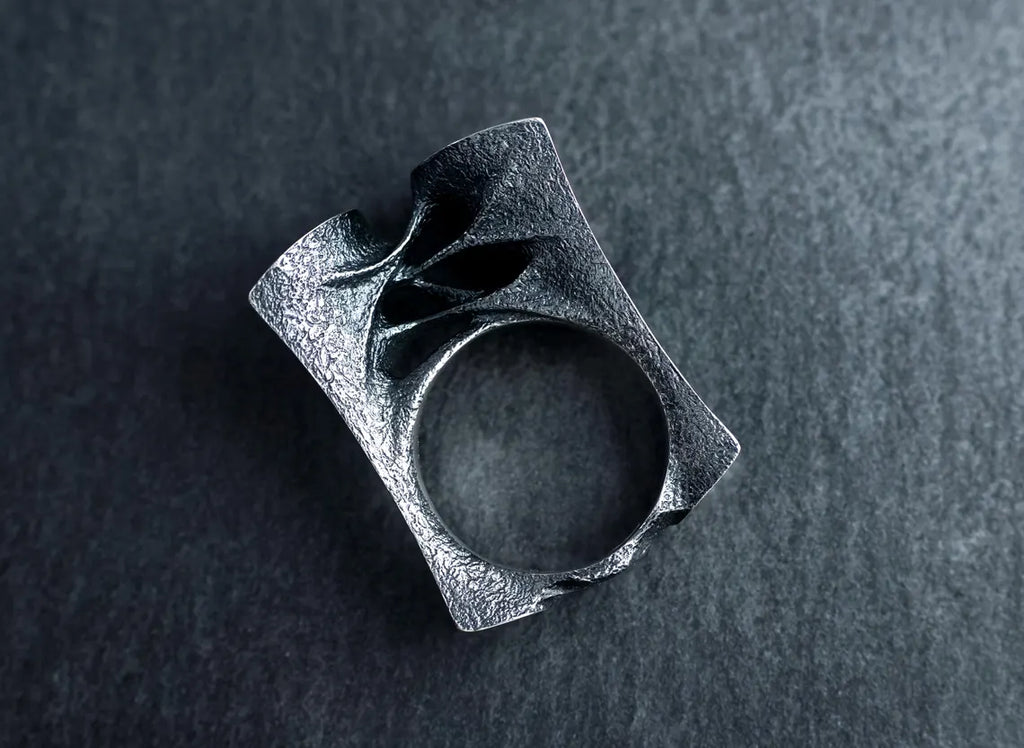 Silver ring with a textured design on a dark gray background
