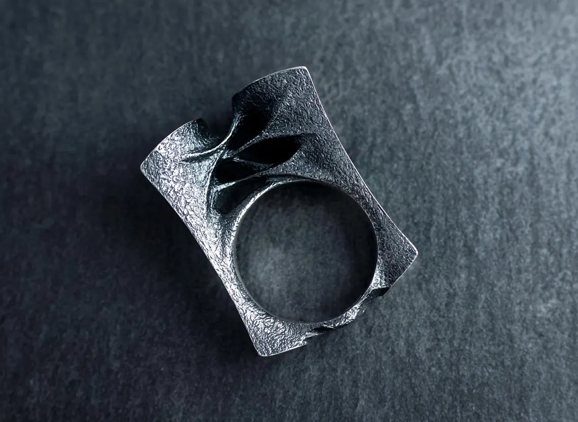 Silver ring with a textured design on a dark gray background