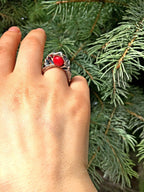 Hand wearing a ring with a red stone against a green leafy background