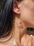 Close-up of a woman wearing a unique earring with a red bead.
