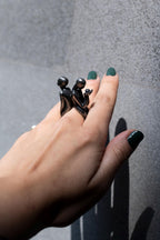 Hand wearing a unique ring with black figurines on a gray background