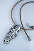 Silver horse head pendant on a brown leather cord against a white background