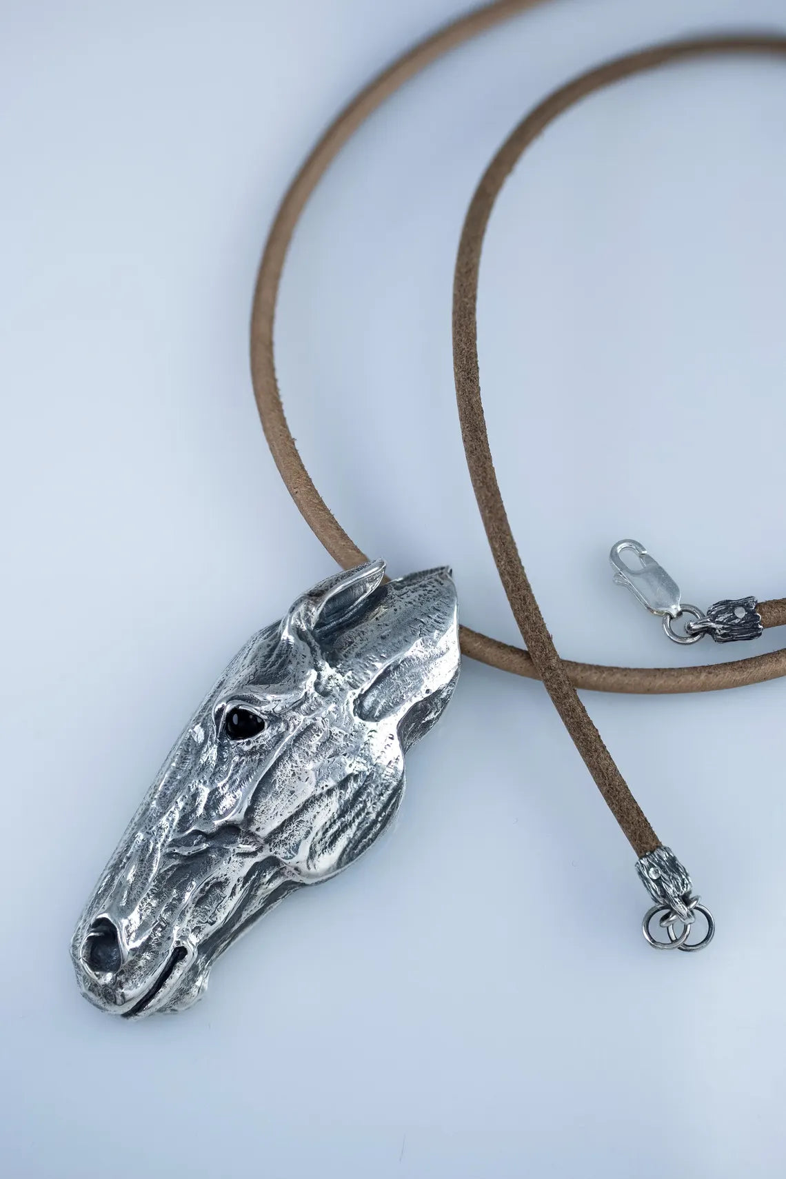 Silver horse head pendant on a brown leather cord against a white background