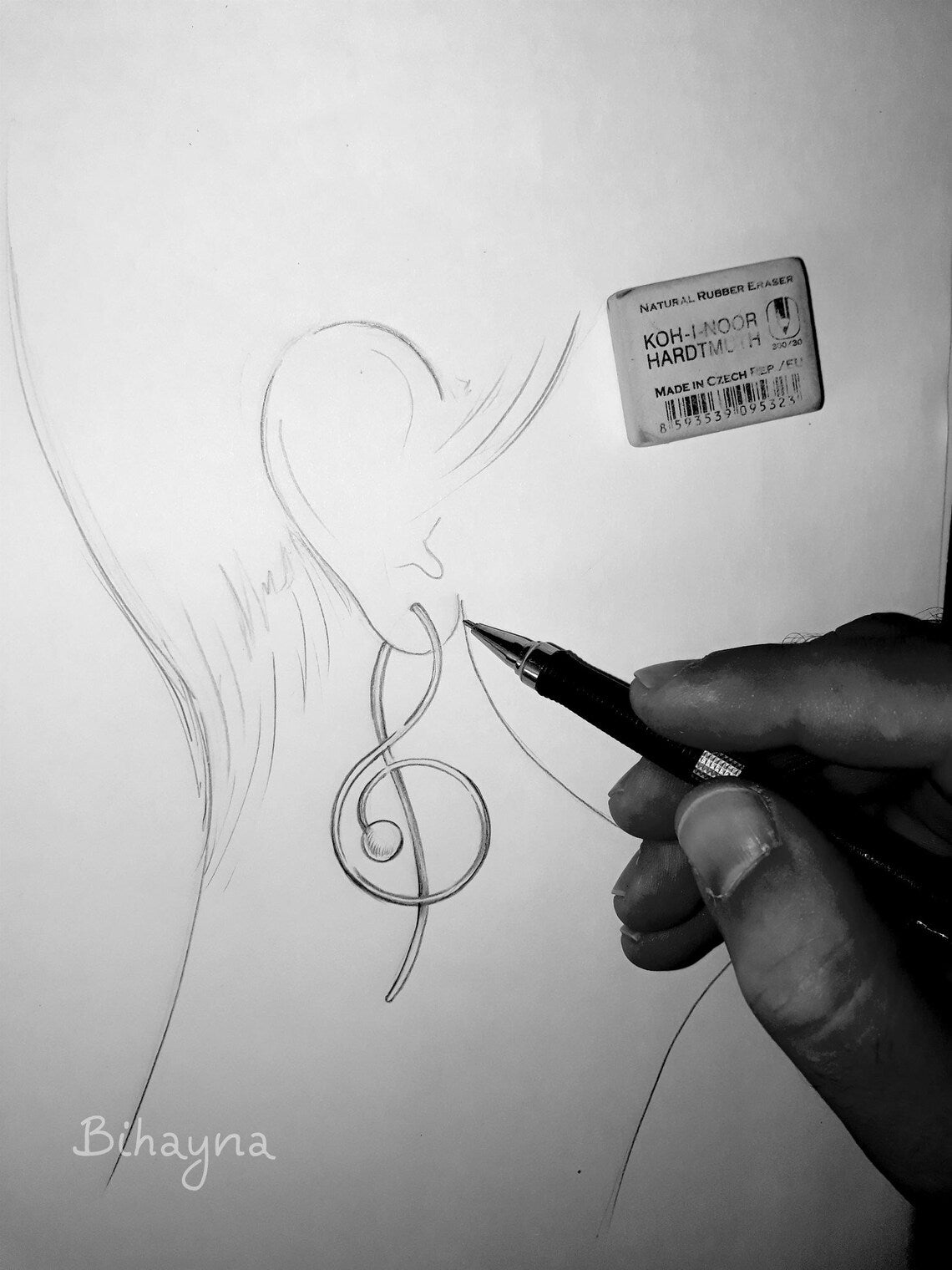 Hand drawing a treble clef symbol on paper with a pen.