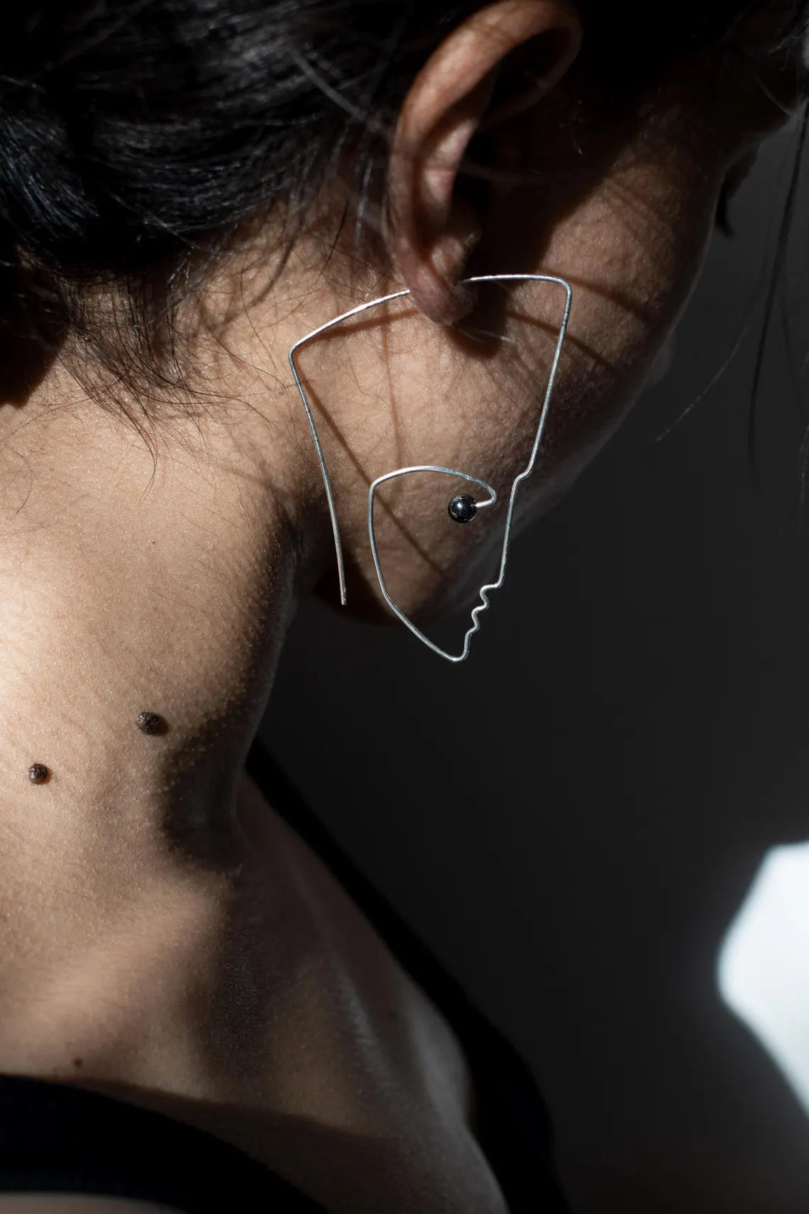 Close-up of an ear wearing a unique wire earring with a dark background