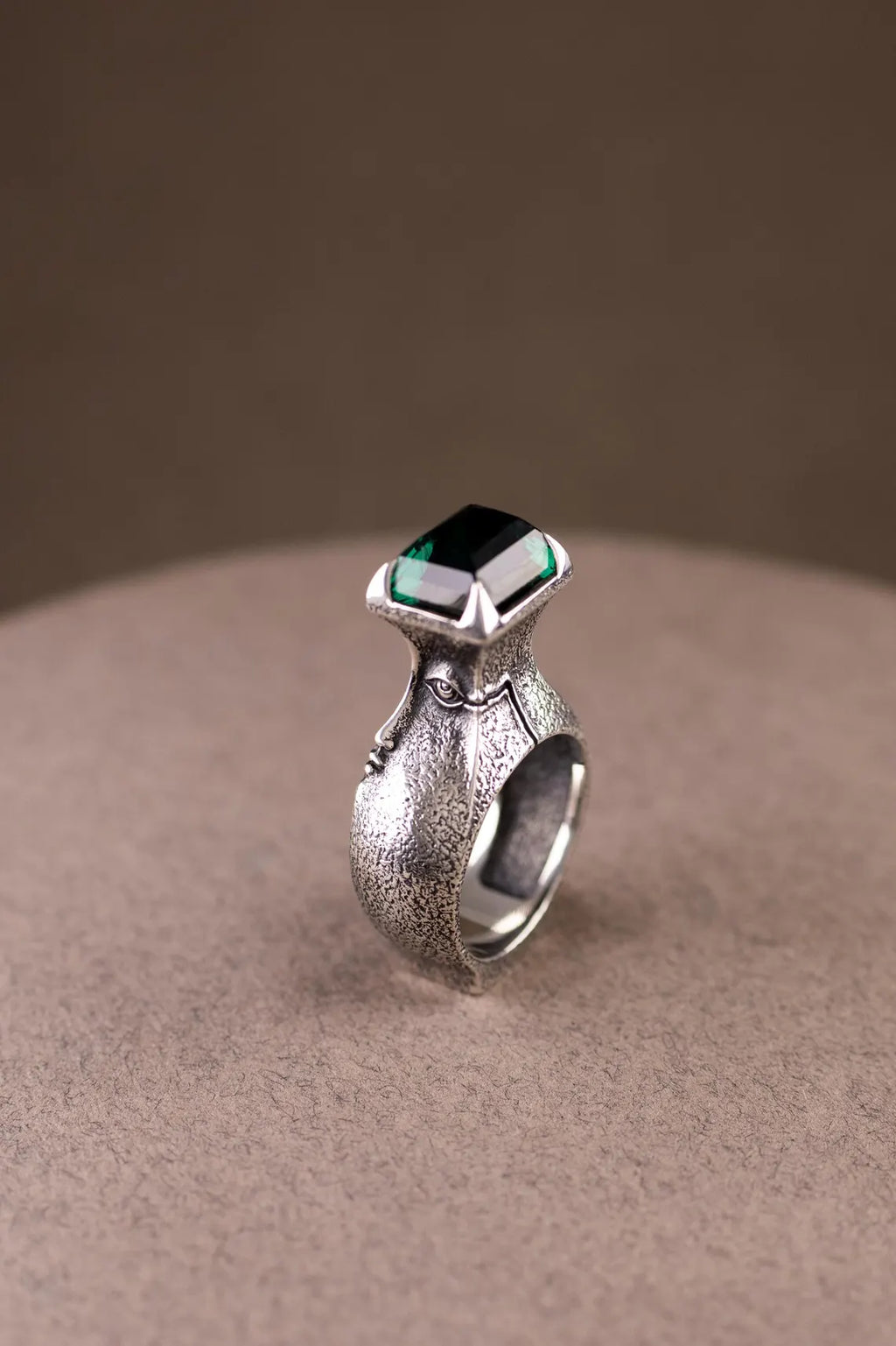 Silver ring with a green gemstone on a beige surface