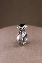 Silver ring with a green gemstone on a beige surface