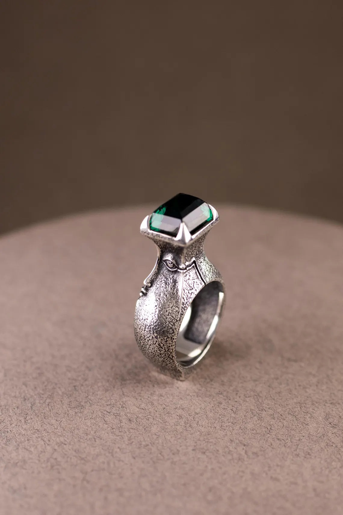 Silver ring with a green gemstone on a beige surface