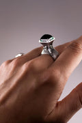 Close-up of a hand wearing a silver ring with a black gemstone on a neutral background