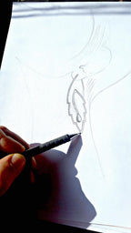 Hand holding a pen over a white sheet of paper with a partially completed design.