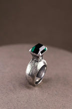 Silver ring with a green gemstone on a beige surface