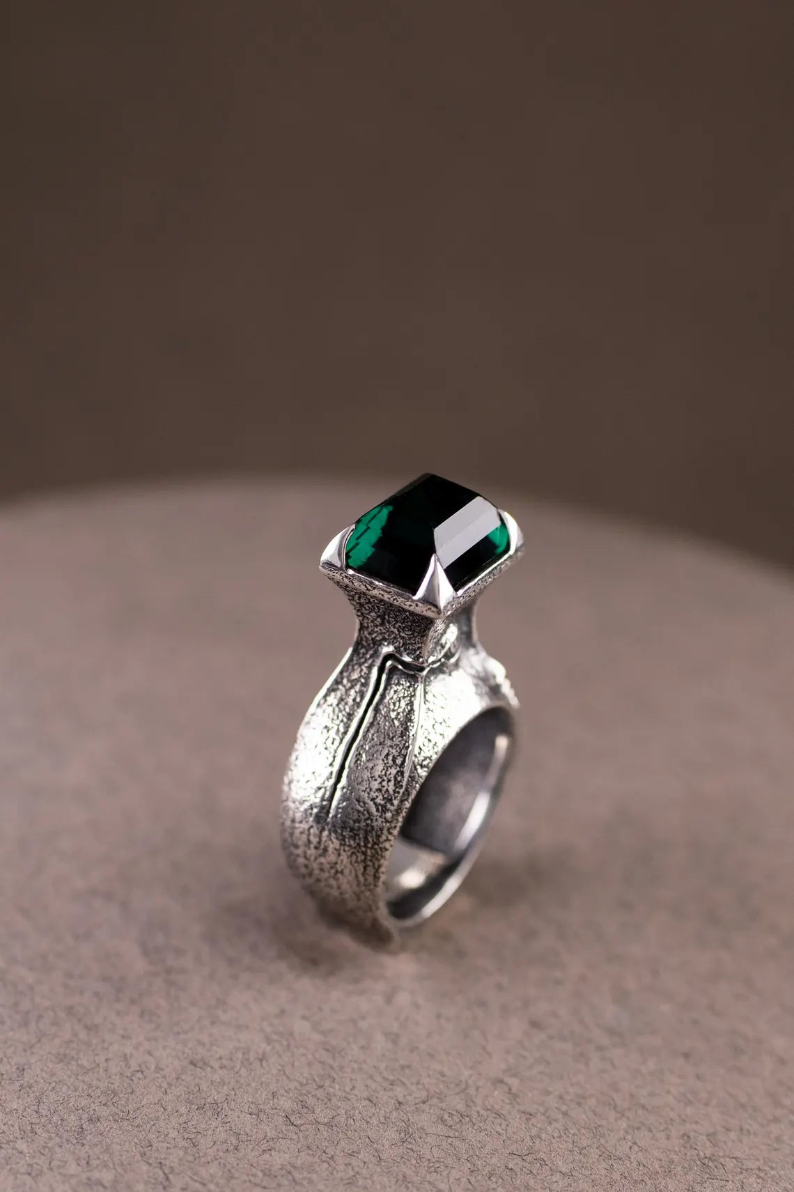 Silver ring with a green gemstone on a beige surface