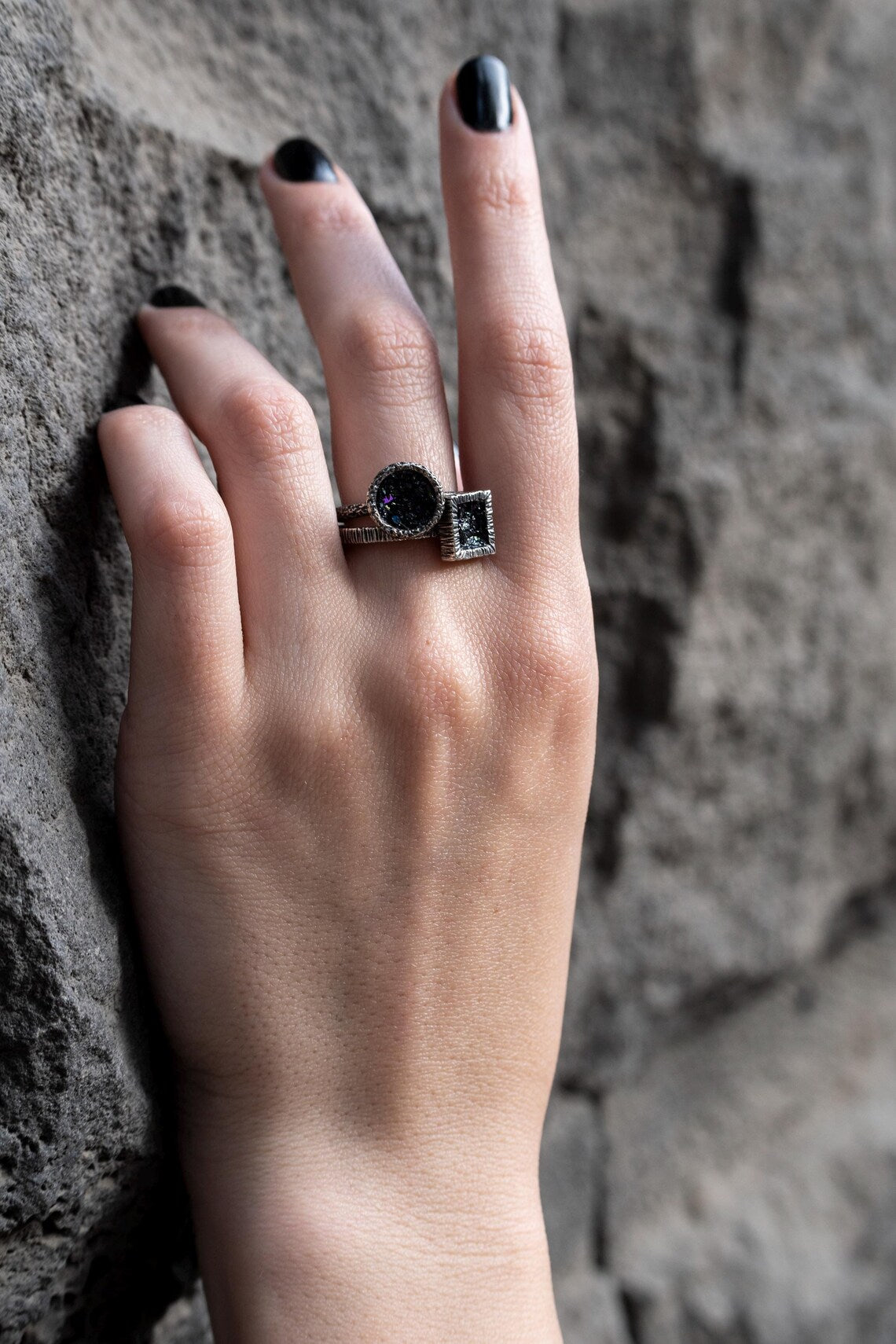 Hand wearing a ring with a dark stone against a textured stone background