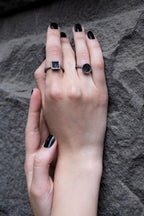 Close-up of two hands with black nail polish and rings on a textured gray background