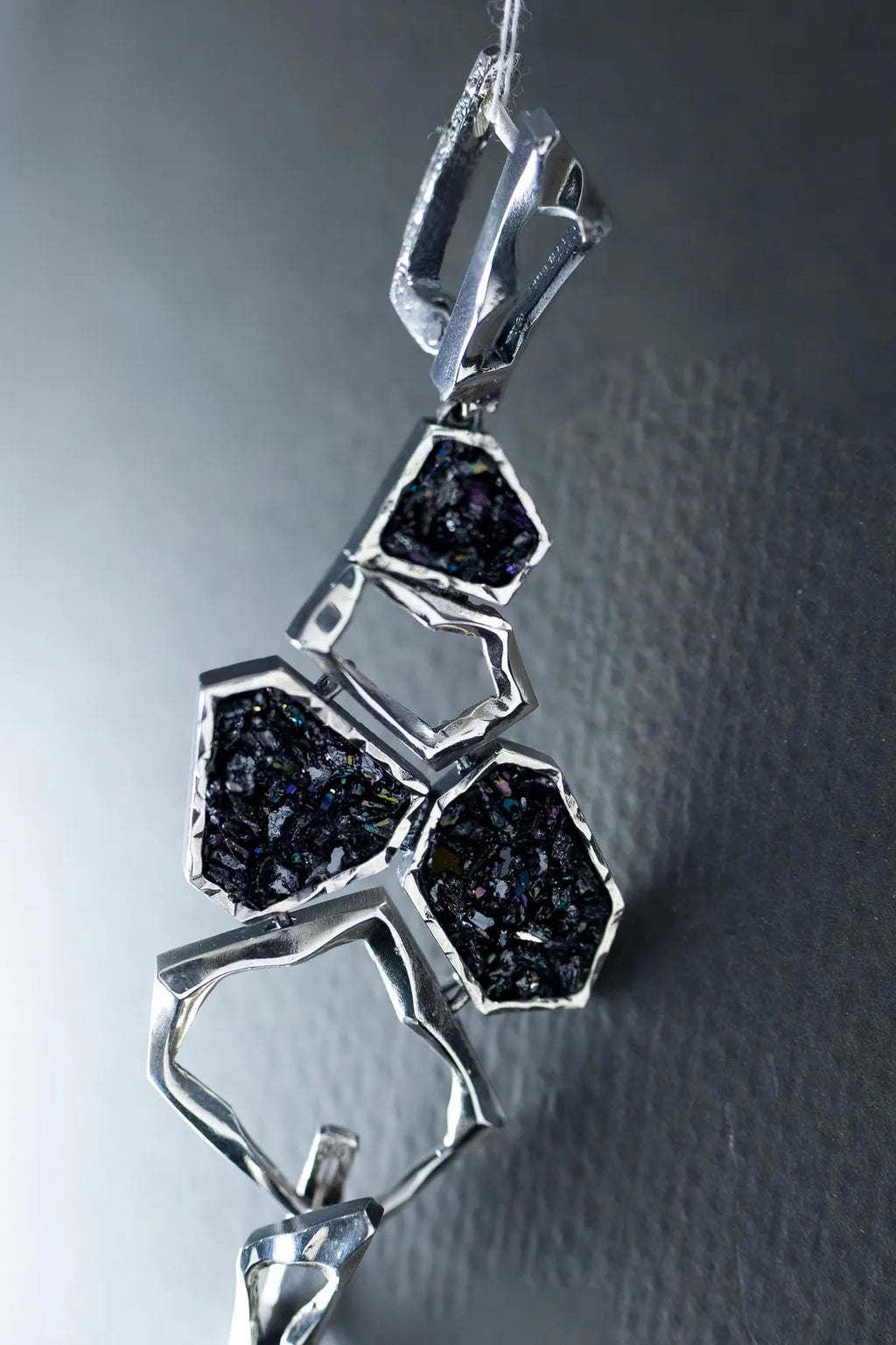 Silver pendant with black gemstones on a textured gray background