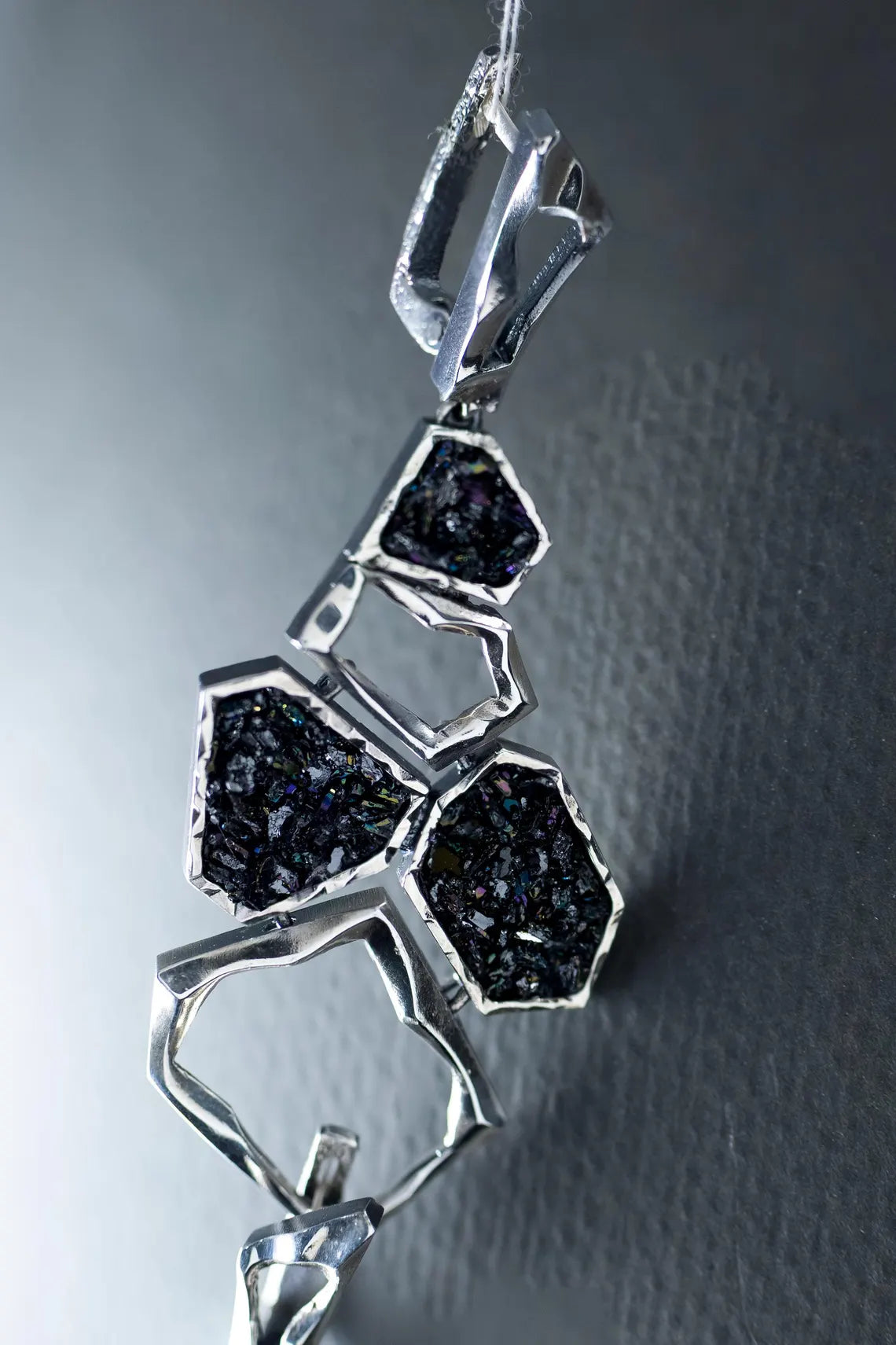 Silver pendant with black gemstones on a textured gray background