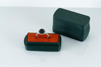 Ring with a black gemstone on an orange cushion inside a green jewelry box with 'BHAYNA' branding.