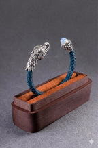 Braided blue bracelet with silver dragon heads in a wooden box on a gray background